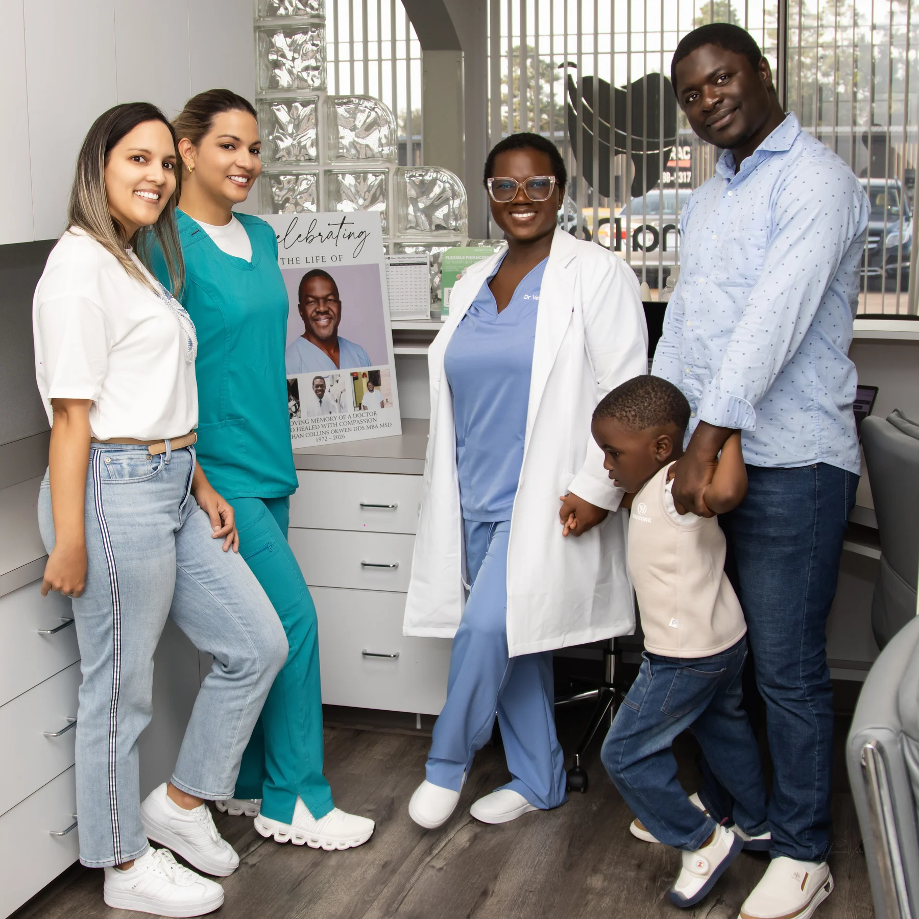 A group gathered at Imma Dental beside the memorial portrait of Dr. Mbachan C. Okwen