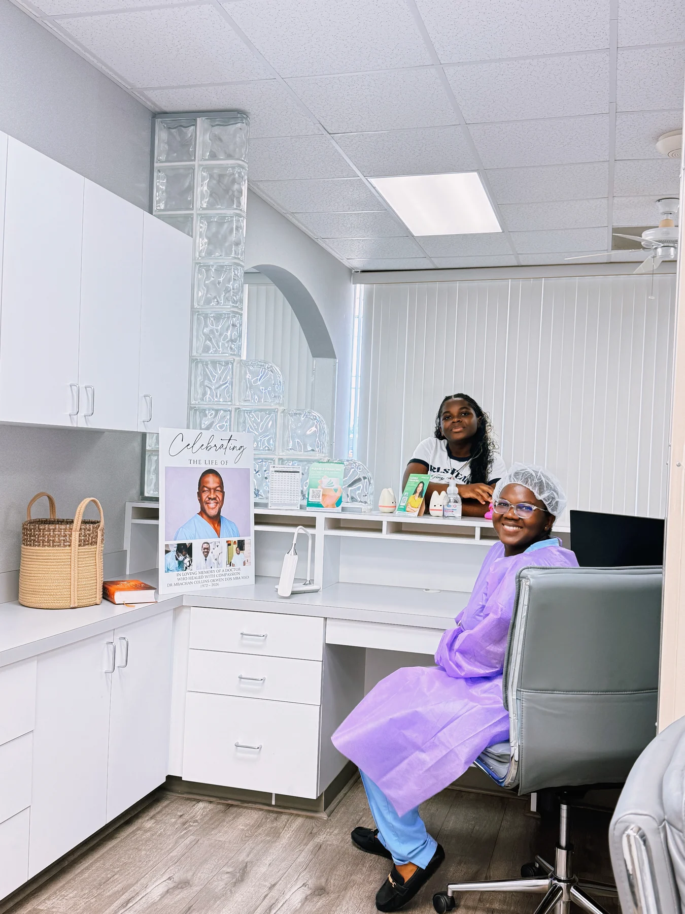 Two people in the Imma Dental reception area beside Dr. Okwen’s memorial display
