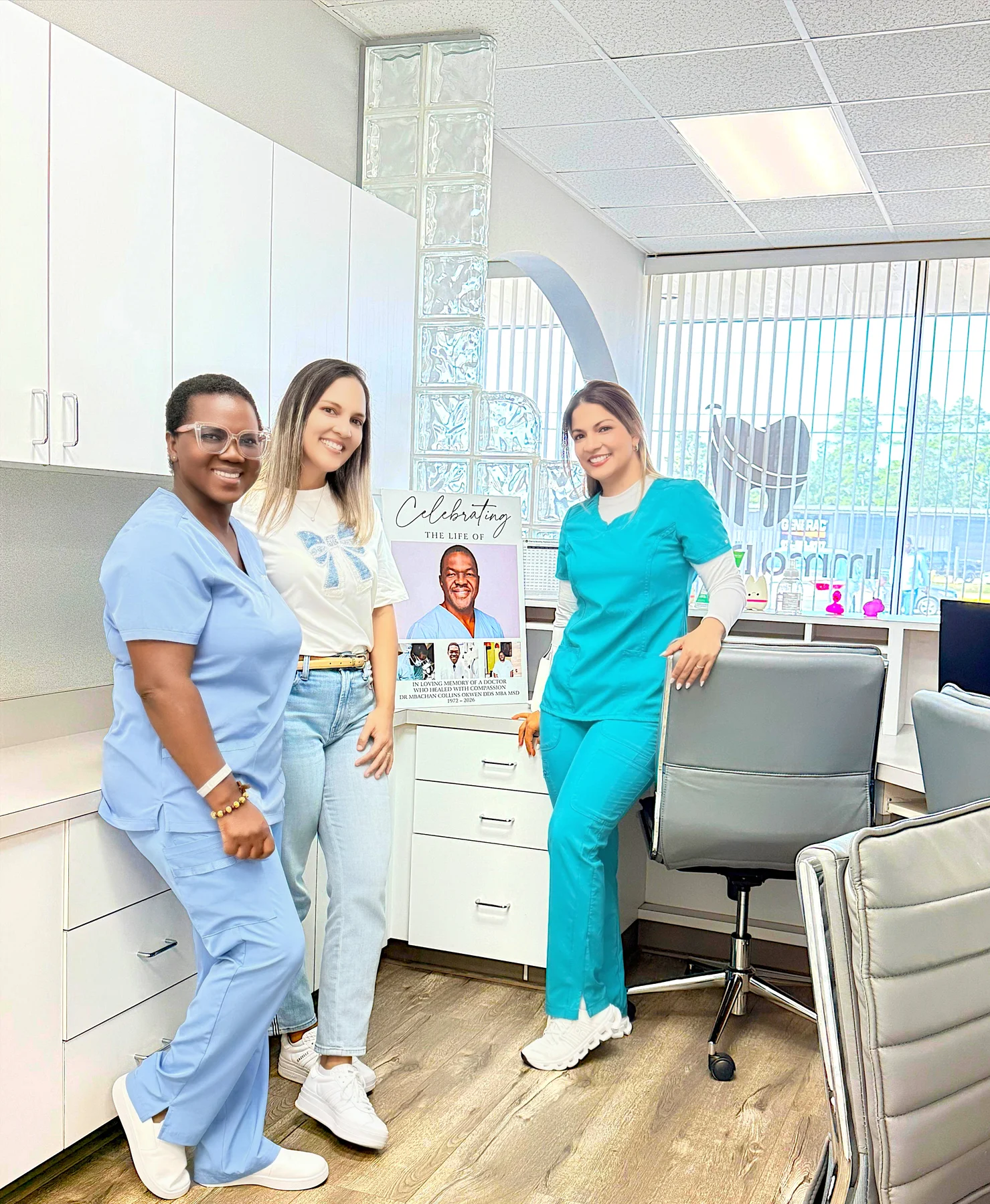 Three team members standing beside Dr. Okwen’s memorial portrait at Imma Dental